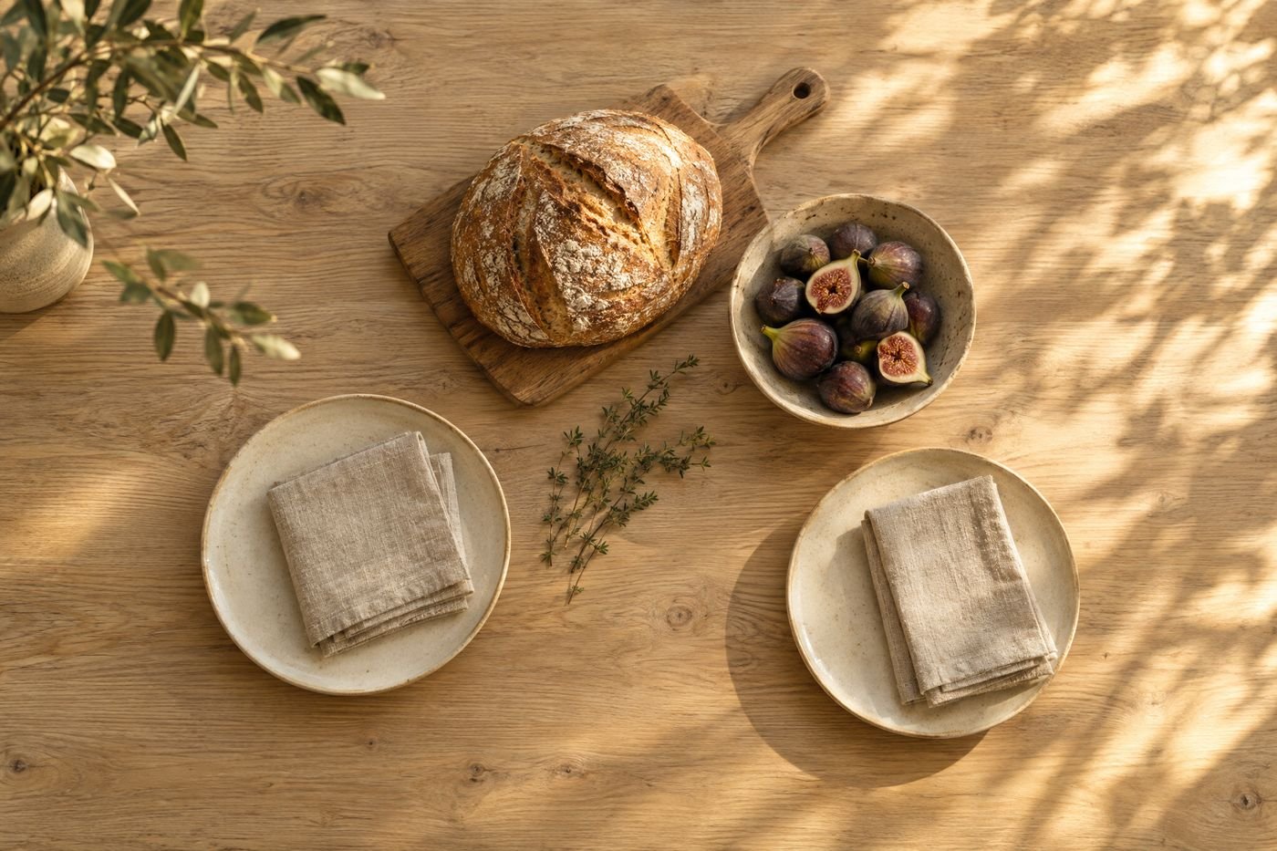 Oak table seen from above, laid for two with a loaf of bread, a bowl of figs, stoneware plates and linen napkins